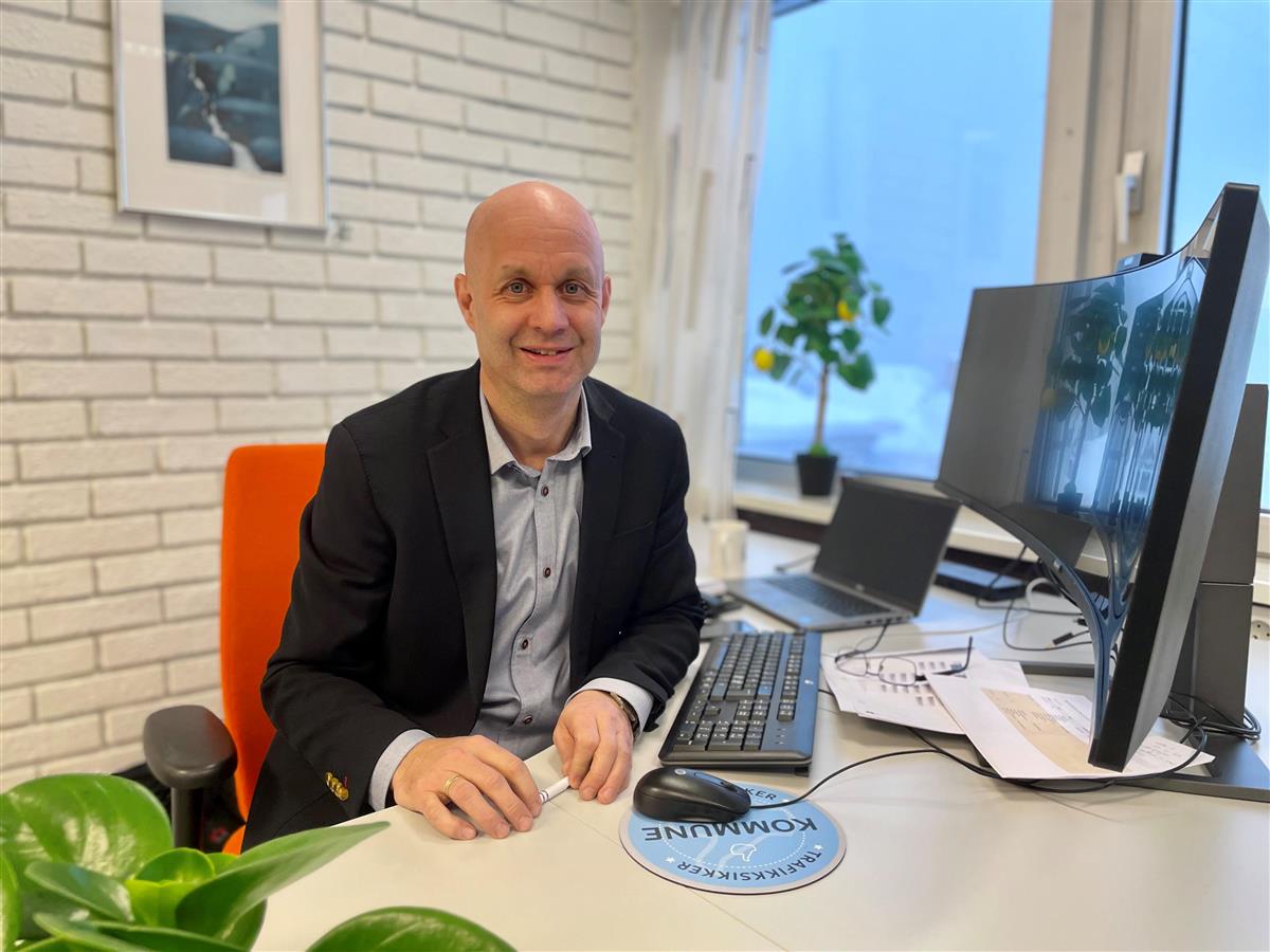 Lars Joakim Tveit sitter smilende ved pulten sin på kontoret sitt - Klikk for stort bilde