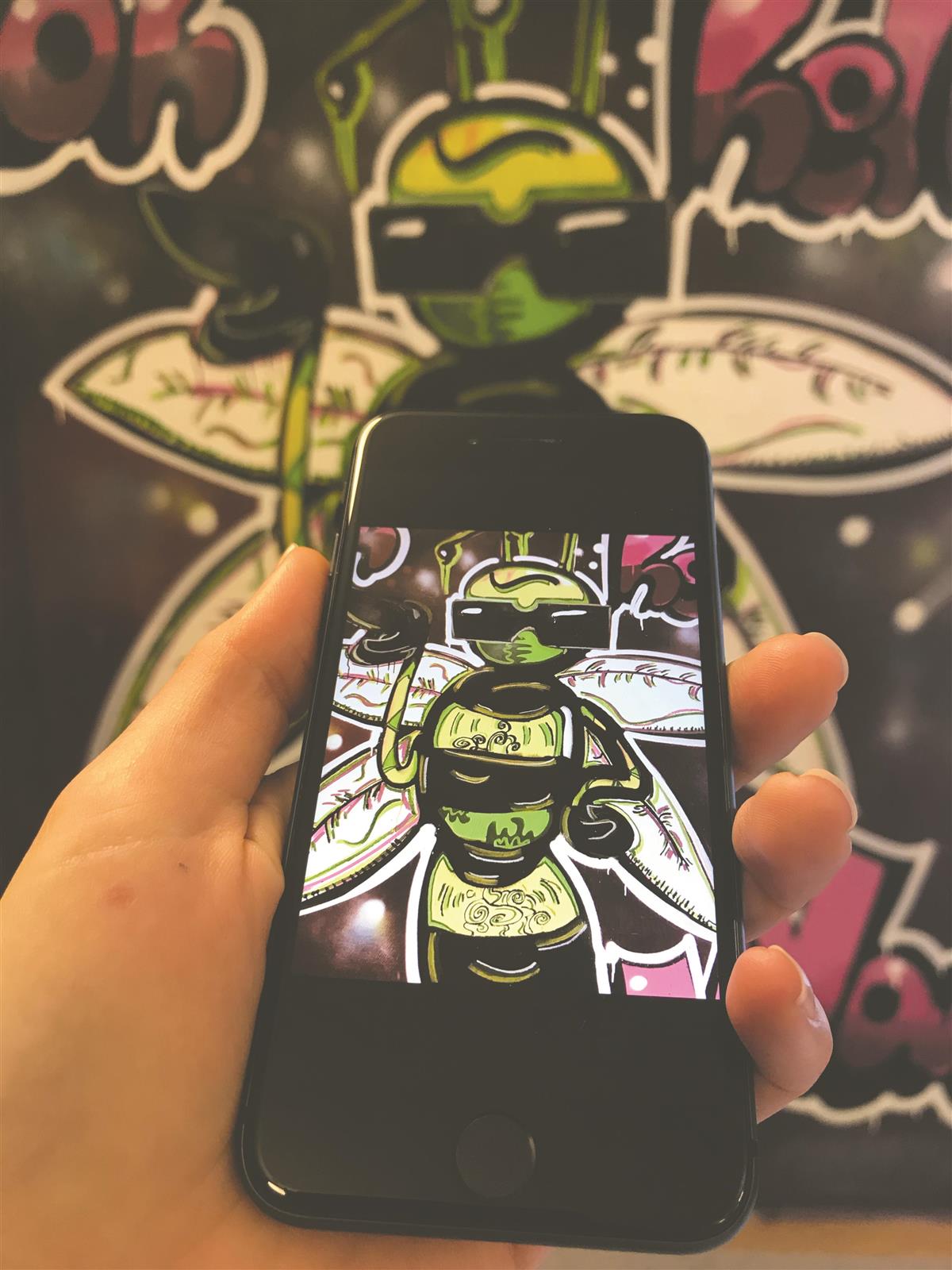 Mobiltelefon og vegg som viser graffitikunst på Backergården - Klikk for stort bilde
